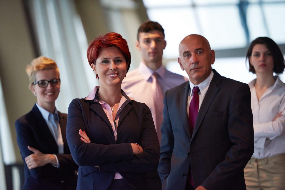 diverse business people group standing together as team  in modern bright office interior  with redhair senior woman in front as leader
