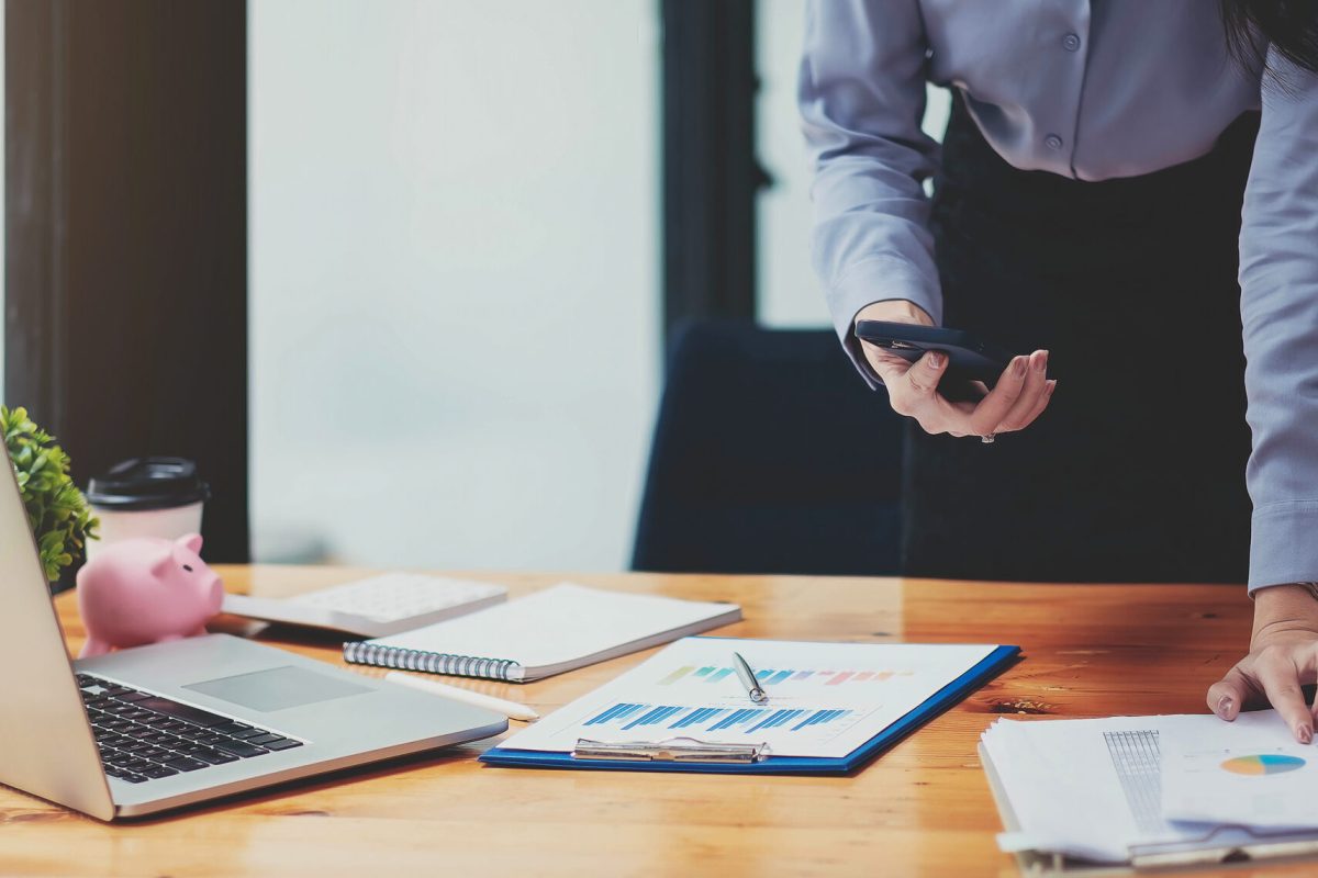 close up view of hands women using smartphone and laptop analyzed financial statements, business document, chart and graph paper, marketing report, accounting, investor, work from home concept.